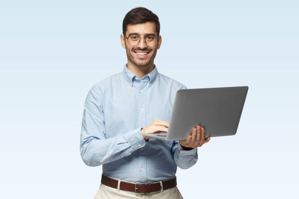 istock Handsome man using laptop and looking at camera with smile, isolated on blue background 1431058030