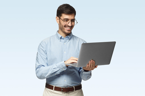 Portrait of young businessman standing, holding laptop and watching media with happy smile, sharing web content