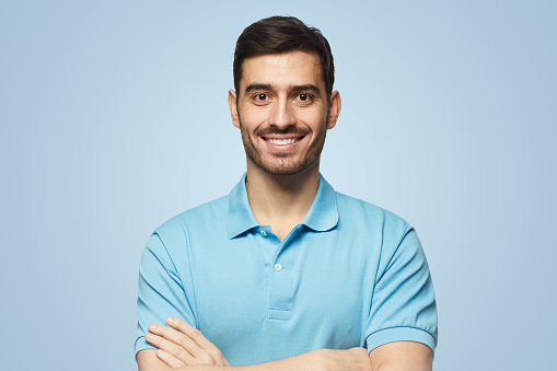 Portrait of smiling handsome man in blue polo shirt, standing with crossed arms isolated on blue background