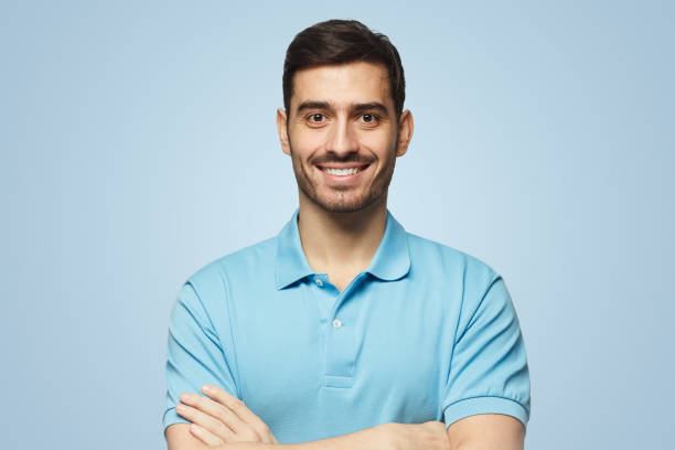 retrato de homem bonito sorridente de camisa polo, de pé com os braços cruzados no fundo azul - blue polo shirt - fotografias e filmes do acervo