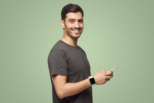 istock Handsome man dressed in gray t-shirt, holding phone, looking at camera on green background 1431059421