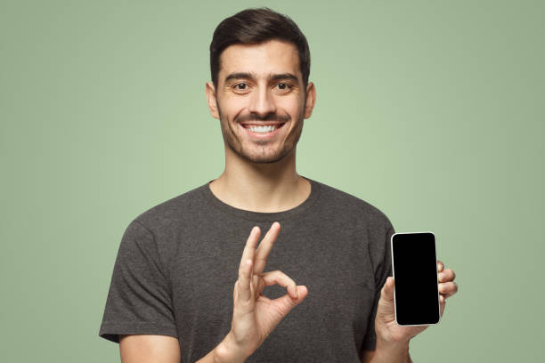 istock Smiling young man holding phone with empty black screen, showing ok gesture with one hand 1431059434