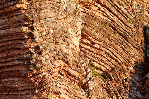 Sunlit rock cut with lines and rows. Geological background texture
