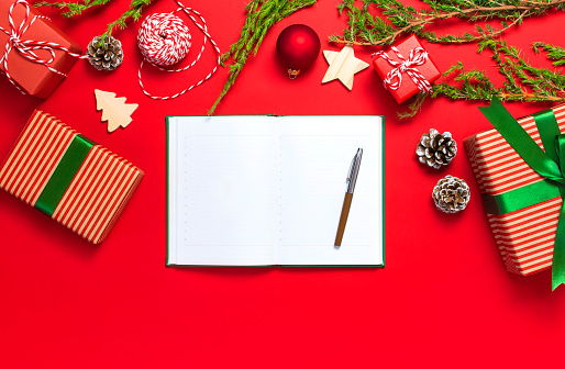 Open notebook with blank pages, gift boxes, fir branches on red background flat lay top view. Christmas planning concept Holiday decorations 2019 Goals. New Year Christmas, winter decoration