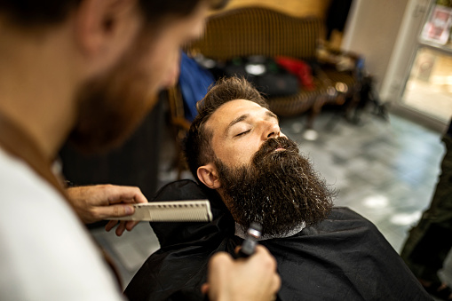 Hairdresser cutting strand of man's beard