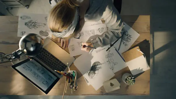 Young woman working on a storyboard in a design studio. A laptop and stationary jar on the table. Woman drawing sketches as a roadmap for the video.