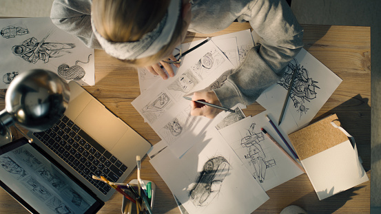 Young woman working on a storyboard in a design studio. A laptop and stationary jar on the table. Woman drawing sketches as a roadmap for the video.