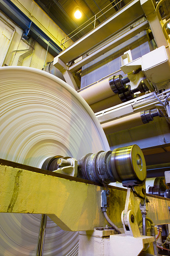 Big rolls of paper coming out of the machinery in a paper mill plant.