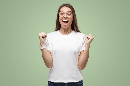 Young excited female shouting to support her favorite team or winning lottery, isolated on green background