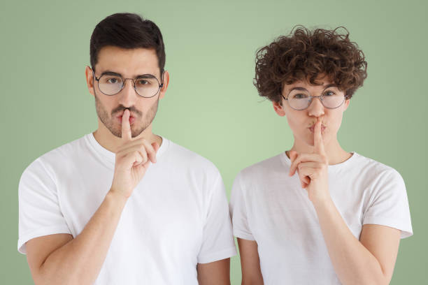 istock Young couple showing shh gesture on green background 1431072733