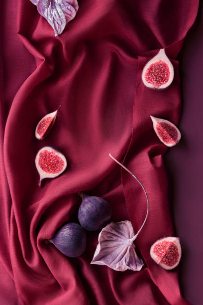 Fresh halved fig fruits and metallic cala flower on vine red silk textile background. stock photo