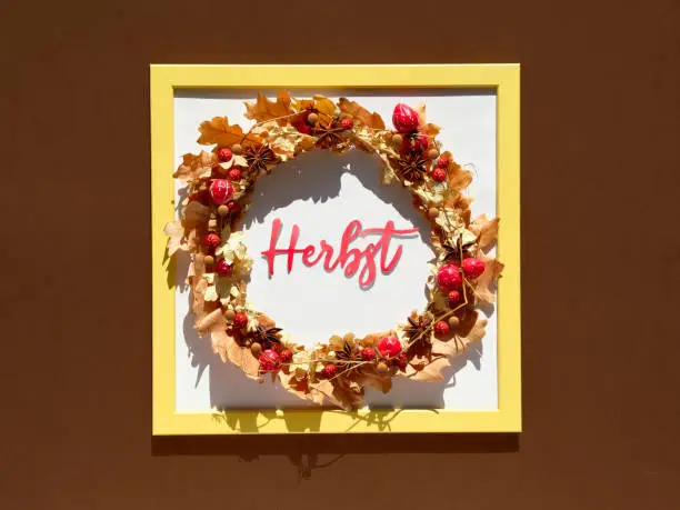 Frame with floral wreath. Boho wreath made of dry Autumn leaves and berries. Word Herbst means Autumn in German language. Seasonal Fall flat lay, top view on brown paper background.