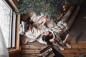 Young stylish love couple girl, guy lie on skin on floor in cozy wooden country house,chalet in winter forest. Celebrating new year eve. Gifts,family holiday.Romantic weekend.Decorated Christmas tree