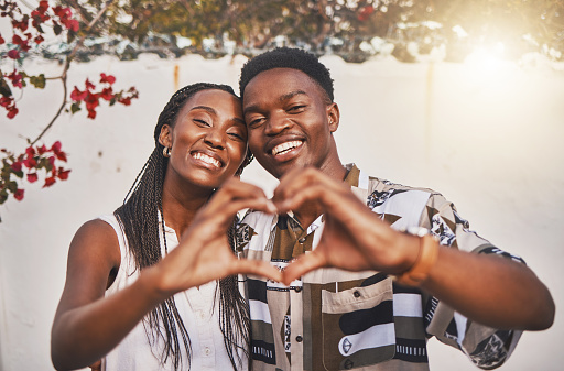 Happy, carefree and excited couple making the heart love sign with their hands posing for a picture or photo. Loving and young African American lovers having fun together smiling in joy