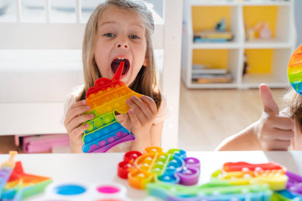 Little girl,kid,child plays with colorful pop it children's room, bedroom.Funny trendy silicone antistress colorful sensory push toy popit.Flapping fidget.Rainbow color.Cure of autism.Stress reliever. niña, niño, niño juega con colorido pop en la habitación de los niños, dormitorio. divertido moderno silicona antiestrés colorido juguete sensorial de empuje popit. agitando inquieto. color arco iris. cura del autismo. calmante del estrés