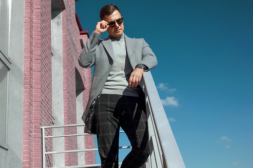 Low angle view of hardened man in gray autumn coat and sunglasses against emerald sky