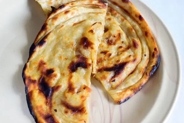 Photo of Closeup of butter paratha or parantha or parotta, a multi layered Indian flat bread generously smeared with freshly churned home butter.