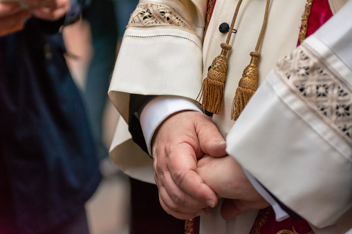 Close Up Of Crossed Chubby Hands Of A Priest On Blurred Background