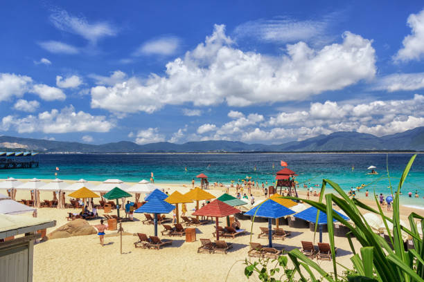 multitud de personas de vacaciones en la playa con cielo azul y nubes blancas - isla de hainan fotografías e imágenes de stock