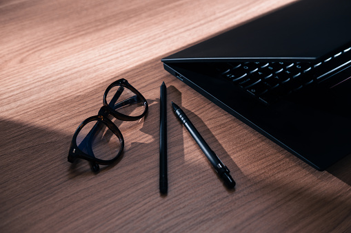 Modern elegant office, close up on laptop, eyeglasses, pen.