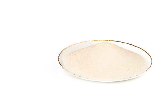 White sugar on a plate over a white background.Ingredient for cake ,cookies ,ice cream and for preparing many other sweet desserts.