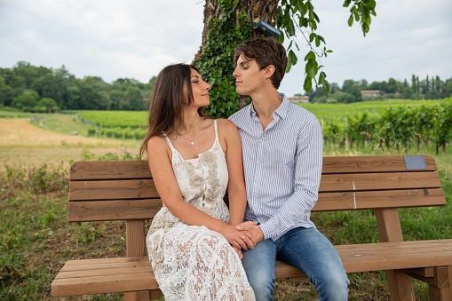 Two lovers look tenderly into each other's eyes while sitting on the bench during a walk in the countryside.