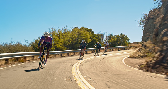 Vehicle mounted shot of a middle-aged African-American man wearing lycra cycling clothes leading a group of cyclists on a morning ride on a sunny day in the Santa Monica Mountains in Malibu, California.