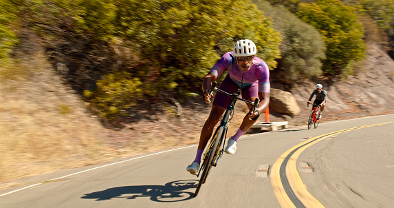 Vehicle mounted shot of a middle-aged African-American man wearing lycra cycling clothes leading a group of cyclists on a morning ride on a sunny day in the Santa Monica Mountains in Malibu, California.