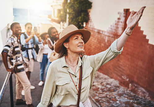 Travel, education and a teacher with students on school field trip, on urban tour. Woman, city guide and group of happy tourists, pointing at local architecture and learning on international holiday.
