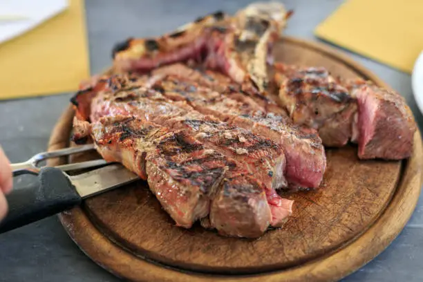 Photo of Cutting Florentine steak, T-BONE STEAK on a wooden board
