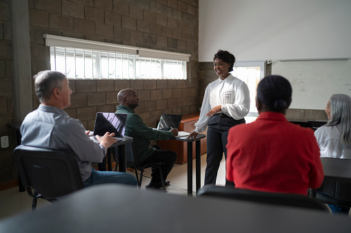 A young female black technology teacher is teaching computing to a multiracial group of senior people (two black man and woman, two white man and woman).