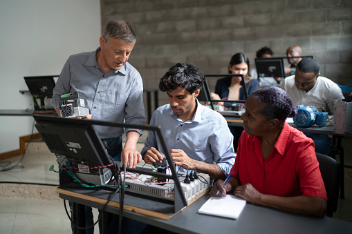A senior professor is giving instructions to some young and senior adult multi racial students during a technology course