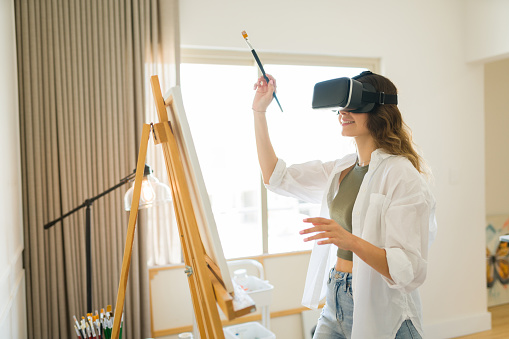 Excited young woman using VR glasses and creating a painting using virtual reality technology