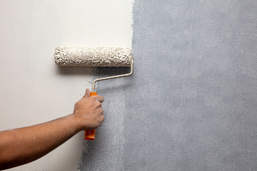 Home painter is painting walls with paint roller