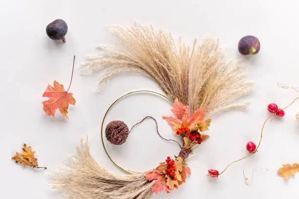 Dried floral wreath from dry pampas grass and Autumn leaves on metal frame with cord.Orange maple leaves. Flat lay on white table, soft natural sunlight.