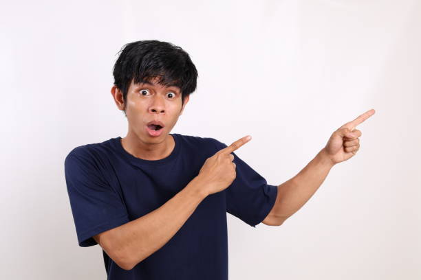 istock Surprised asian young man standing while pointing sideways. Isolated on white background with copyspace 1431150913