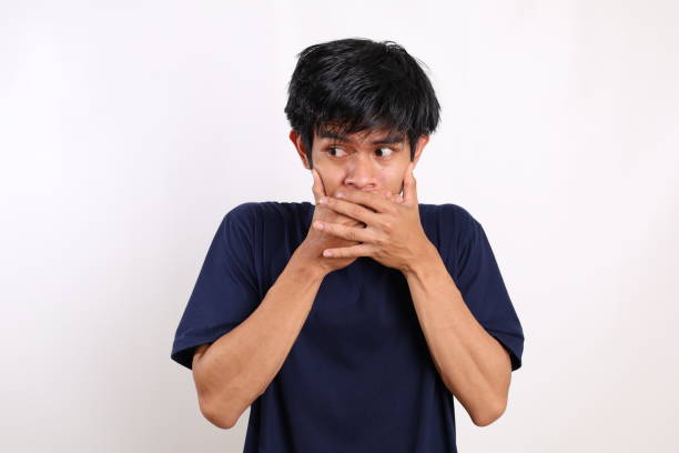 istock Asian young man covering his mouth while glancing sideways. Isolated on white background 1431150937