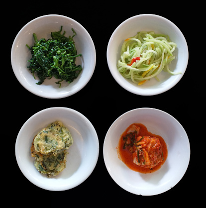 Assorted Korean Side Dishes - Kim chi cabbage, Sigeumchi Namul or seasoned spinach, sliced Chayote and Pajeon vegetable fritters