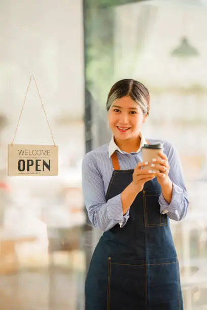 Photo of Asian women set up a sign to open a shop to welcome customers at a coffee shop. small business owner and startups and coffee shops food and drink concept