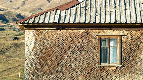 Part of an old two storey wooden cottage with window  in the mountain village with a gray cliff in the background