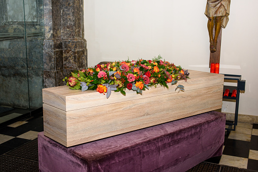 coffin with flowers on it in church with Jezus Christ against the wall waiting to be transported for the service