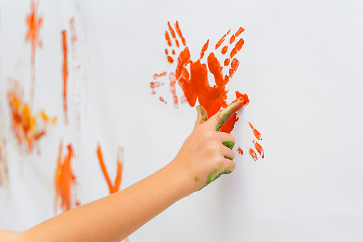 A child's hand draws red paint on the wall. The kid's finger is painting on white paper