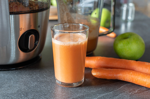 Homemade fresh squeezed carrot juice with green apple. Served on kitchen table background with juicer