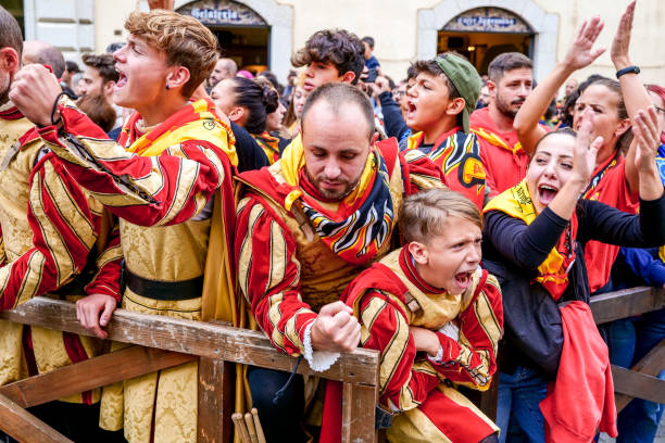 The exultation of some supporters in period costume during the Palio in the medieval town of Gualdo Tadino Gualdo Tadino, Umbria, Italy, October 02 -- A scene from the traditional Palio di San Michele Arcangelo (Palio of St Archangel Michael) in the medieval town of Gualdo Tadino, in Umbria. An ancient three-day festival that involves the entire community in a traditional Corteo Storico (Historical and Allegoric Parade) and culminates with a donkey race between the four 'contrada' (districts) of this medieval town. In the photo, the emotion and exultation of some supporters in medieval costume during the Palio races. An important center since Roman times, Gualdo Tadino rises between Foligno and Gubbio along the ancient Flaminia consular road, traced by the Romans. Its history spans the entire Middle Ages and, despite being partially destroyed and sacked several times and placed under the dominion of Perugia, this ancient Umbrian center still retains its medieval charm. The Umbria region, considered the green lung of Italy for its wooded mountains, is characterized by a perfect integration between nature and the presence of man, in a context of environmental sustainability and healthy life. In addition to its immense artistic and historical heritage, Umbria is famous for its food and wine production and for the high quality of the olive oil produced in these lands. Image in high definition format. gualdo tadino stock pictures, royalty-free photos & images