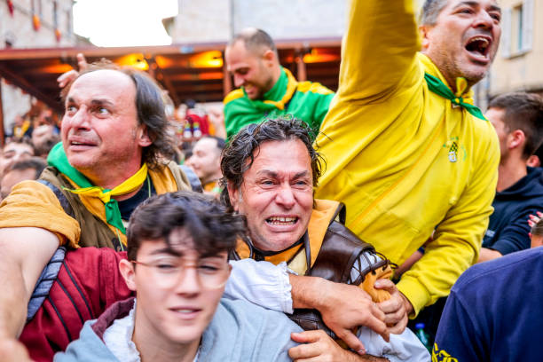 The emotion and exultation of some supporters during the Palio in the medieval town of Gualdo Tadino Gualdo Tadino, Umbria, Italy, October 02 -- A scene from the traditional Palio di San Michele Arcangelo (Palio of St Archangel Michael) in the medieval town of Gualdo Tadino, in Umbria. An ancient three-day festival that involves the entire community in a traditional Corteo Storico (Historical and Allegoric Parade) and culminates with a donkey race between the four 'contrada' (districts) of this medieval town. In the photo, the emotion and exultation of some supporters in medieval costume during the Palio races. An important center since Roman times, Gualdo Tadino rises between Foligno and Gubbio along the ancient Flaminia consular road, traced by the Romans. Its history spans the entire Middle Ages and, despite being partially destroyed and sacked several times and placed under the dominion of Perugia, this ancient Umbrian center still retains its medieval charm. The Umbria region, considered the green lung of Italy for its wooded mountains, is characterized by a perfect integration between nature and the presence of man, in a context of environmental sustainability and healthy life. In addition to its immense artistic and historical heritage, Umbria is famous for its food and wine production and for the high quality of the olive oil produced in these lands. Image in high definition format. gualdo tadino stock pictures, royalty-free photos & images