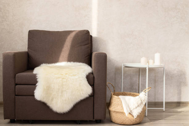 istock A sheep skin on a chair, next to a wicker basket with a blanket and a coffee table with candles. Minimalist interior of the living room. Copy space. 1431286449