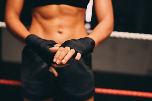 Female boxer wrapping her hands while standing in a boxing ring. Athletic young woman preparing for a boxing training session in a fitness gym.