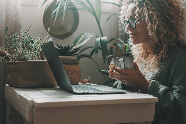 istock One lady using laptop at home drinking tea or coffee in indoor leisure activity online. Pretty woman working on computer and smiling. Lady surfing the web alone with nature plants garden in background 1431297020