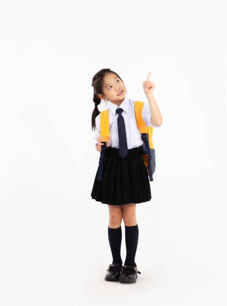 istock Back to school concept. Cute asian junior school student kid in uniform with yellow backpack posing finger pointing on white background. 1431298112