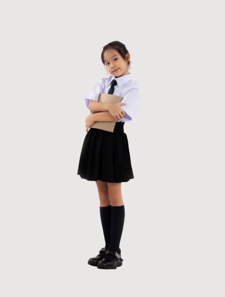 istock Back to school. Asian kid junior school student in british international uniform posing holding book on white background. 1431298243